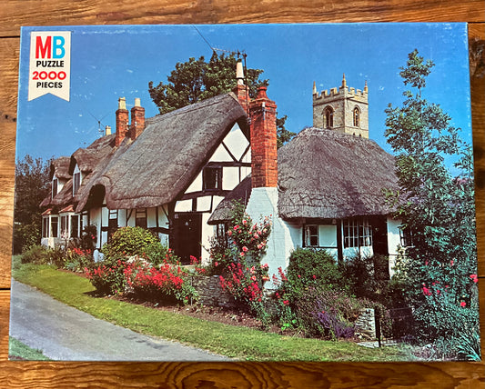 A vintage Milton Bradley puzzle depicting a landscape image of Welford, England, featuring thatched roof houses and a church steeple.