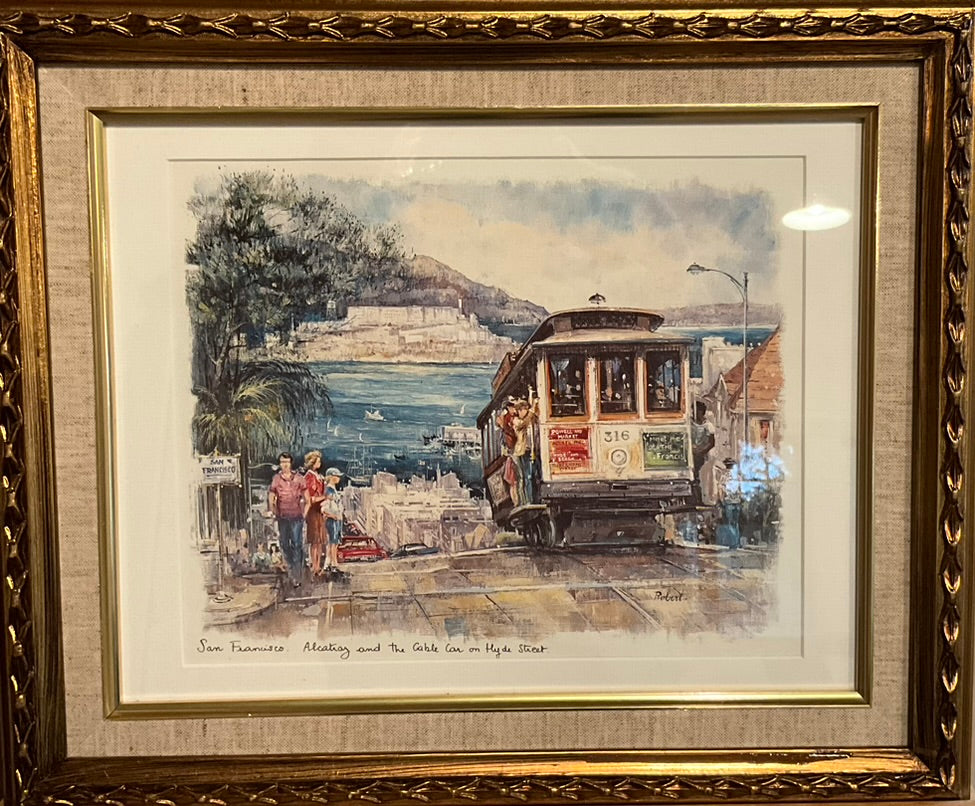 a framed artwork depicting a trolly passing pedestrians on it's way to a the ocean in San Francisco.